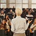 Kvinnelig foreleser med ryggen til foran et fullsatt auditorium