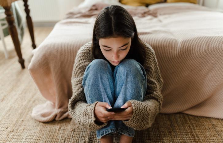Ung jente sitter på gulvet og leser på mobilen sin
