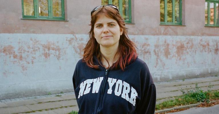 Portrettfoto av Amalie Sehested Rom, stipendiat ved UiO, foran en rosa leiegård med grønne karmer.