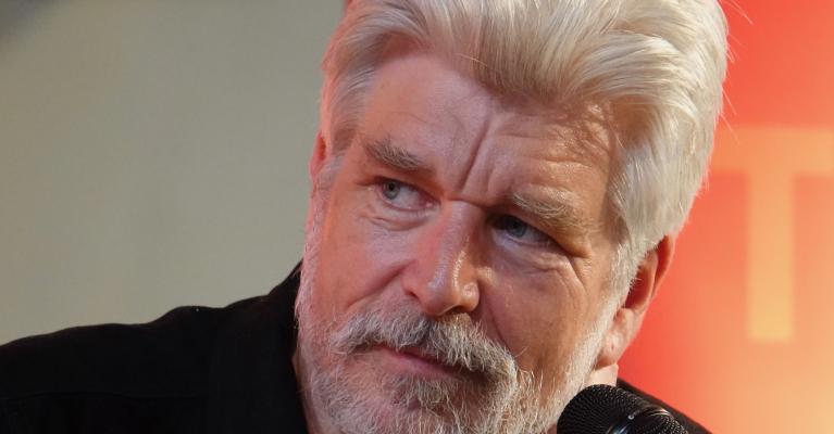 Portrettfoto av forfatter Karl Ove Knausgård med mikrofon mot oransje bakgrunn