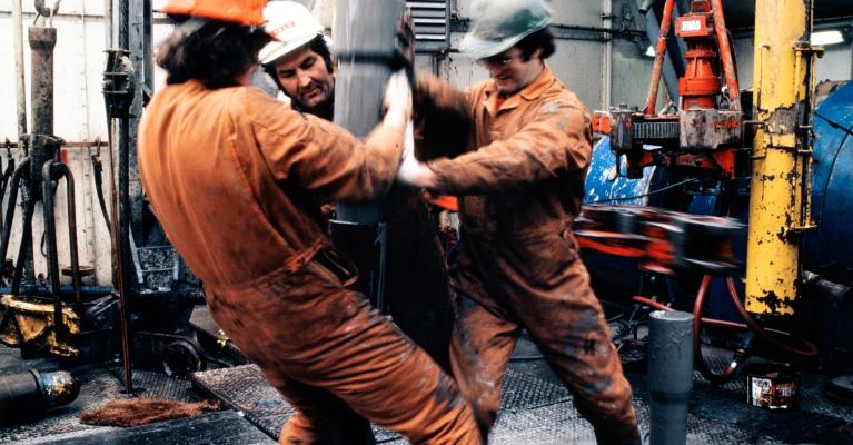 Tre arbeidere i verneutstyr jobber med boring på oljeplattform