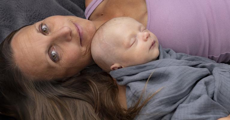 Godt voksen kvinne ligger med sovende baby på brystet