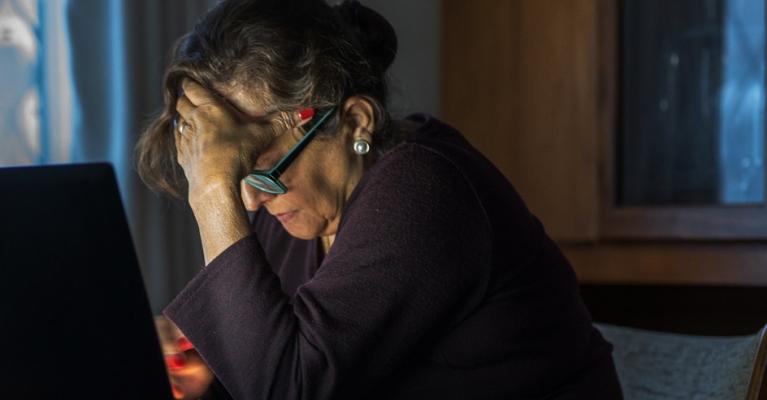 Eldre kvinne med bøyd hode foran pc'n