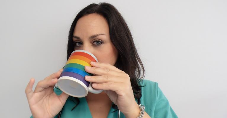 Ung kvinnelig helsearbeider drikker av kopp med regnbueflagg