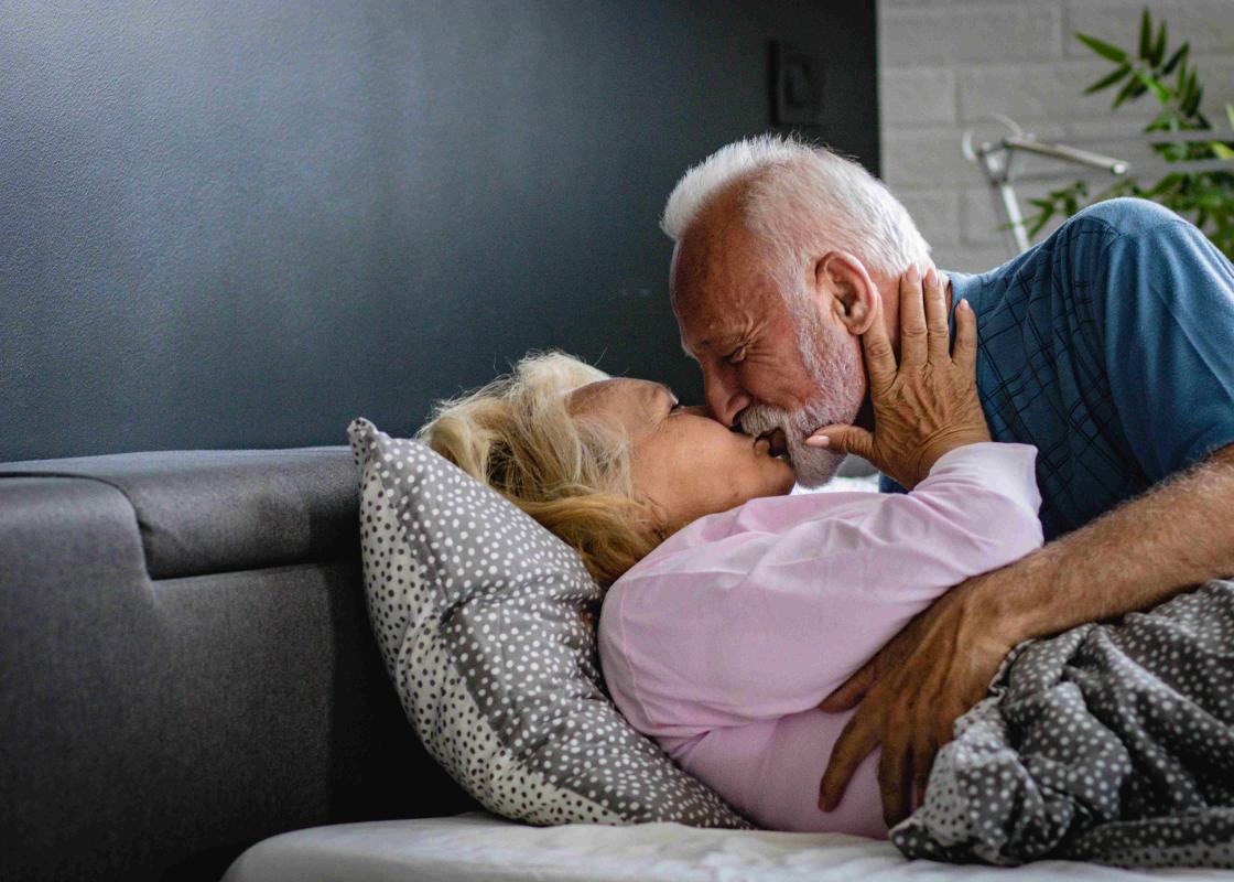 Eldre mann med skjegg omfavner eldre kvinne i en seng