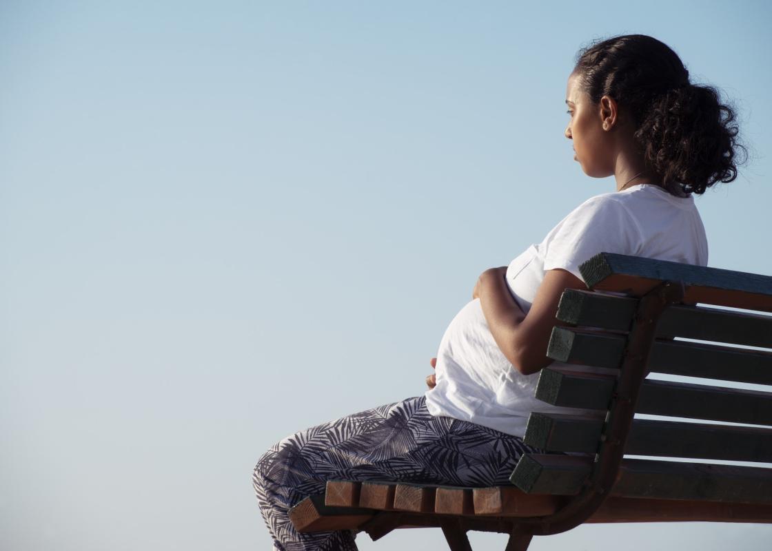 Gravid kvinne sitter på benk med ryggen til