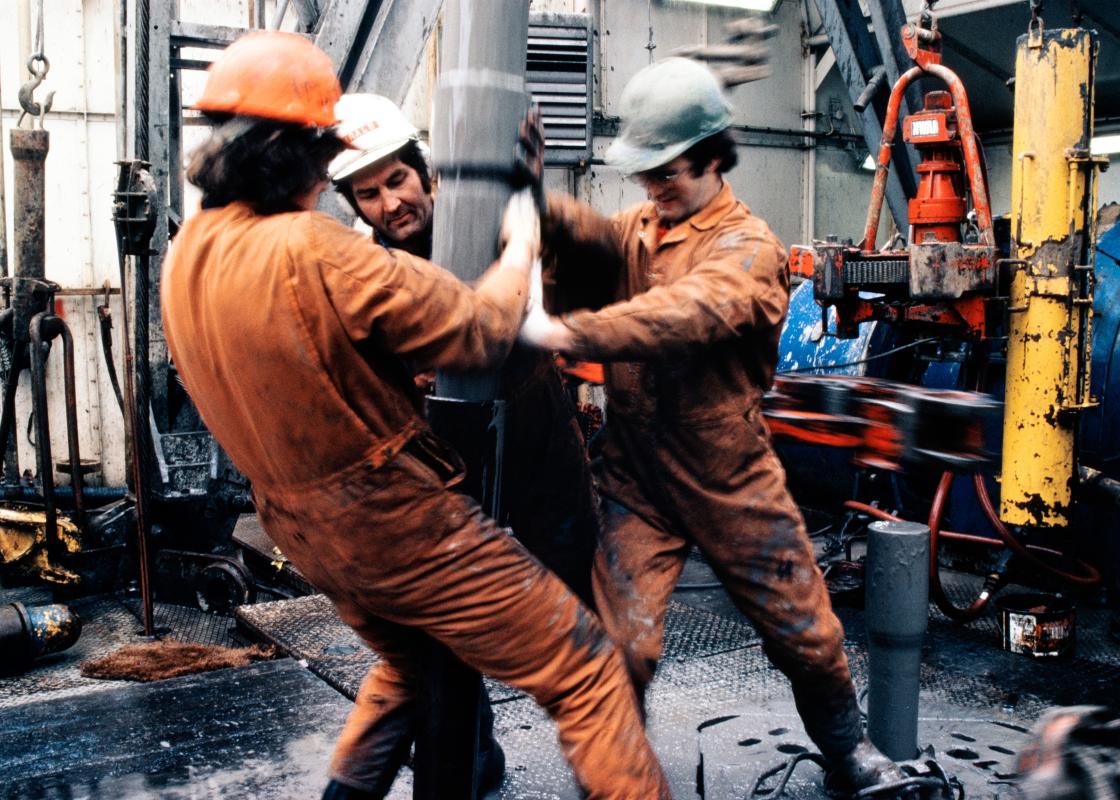 Tre arbeidere i verneutstyr jobber med boring på oljeplattform