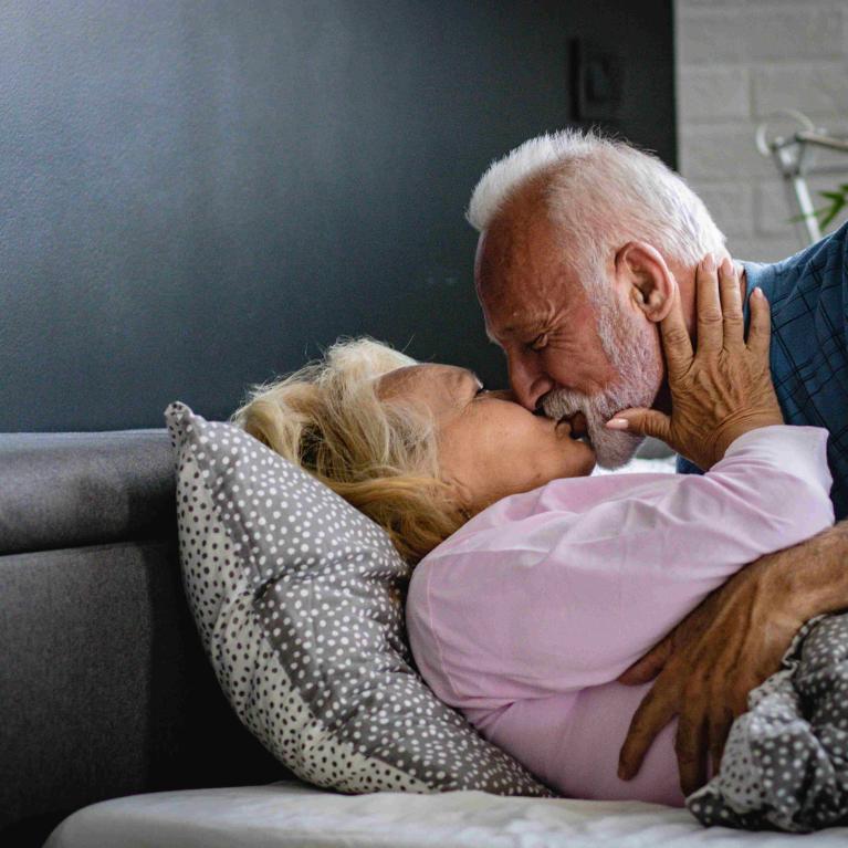 Eldre mann med skjegg omfavner eldre kvinne i en seng