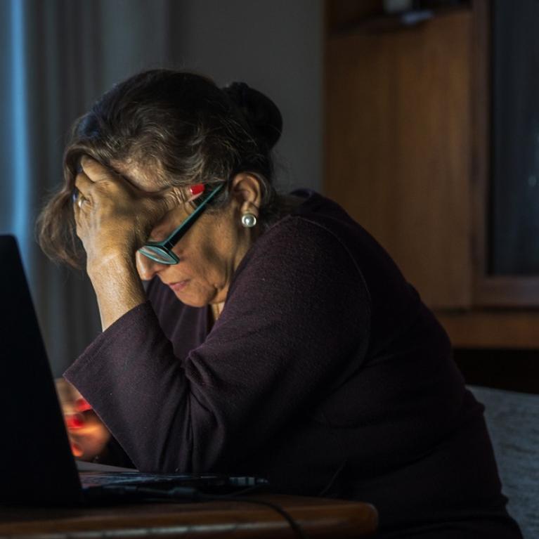 Eldre kvinne med bøyd hode foran pc'n